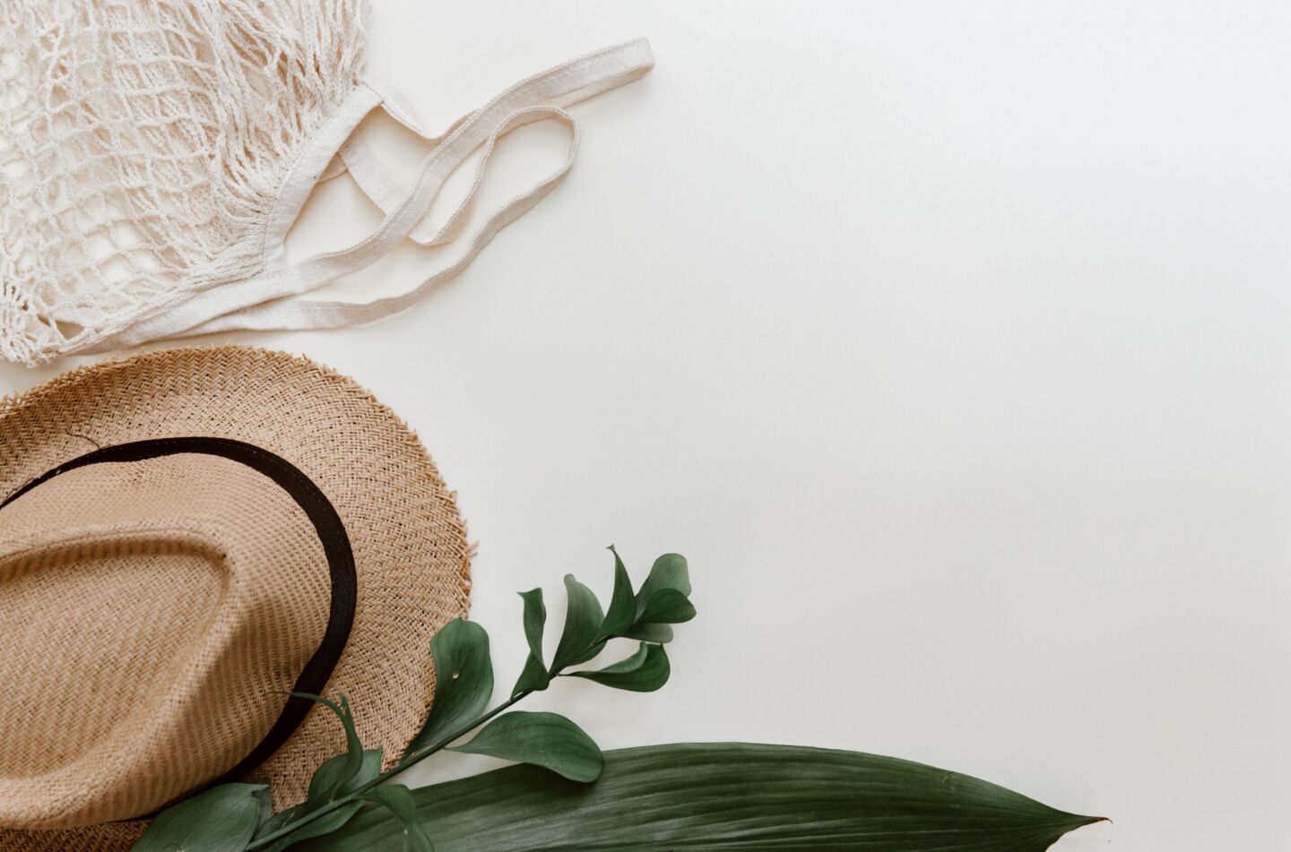 A soft white background with a textile bag, straw sun hat and some green plant leaves to show personal touches as a decorative image.