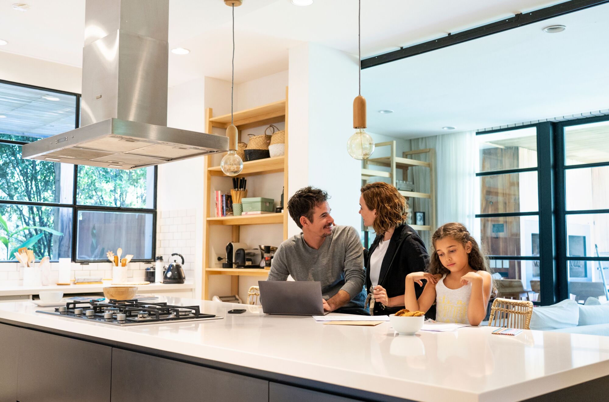 An image that includes a happy couple with a little girl and it shows a slice of their daily activity in the kitchen while they use the kitchen island for different purposes.